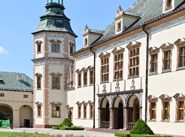 Fotografia jasnego zabytkowego pałacu z wieżą, arkadami i małym dziedzińcem