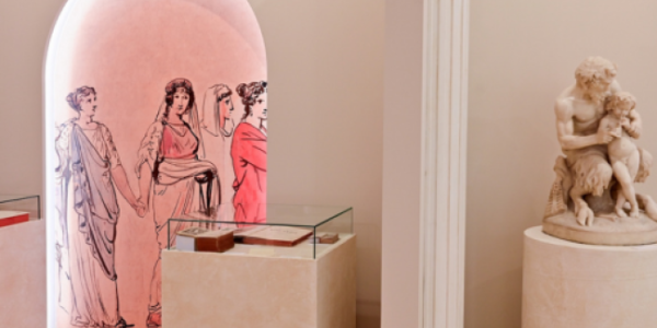 Fotografia: różowy wazon z rysunkami postaci na postumencie, obok mała marmurowa rzeźba