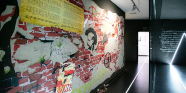 Kolorowy mural na ceglanej ścianie w galerii; ciemny korytarz z neonowym trójkątem