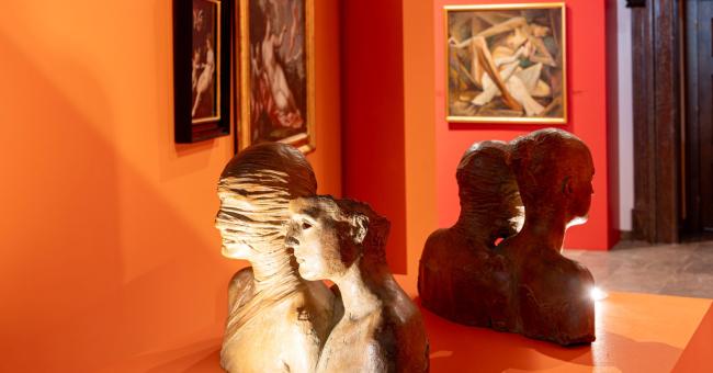 Fotografia dwóch kamiennych popiersi na pomarańczowej powierzchni w galerii