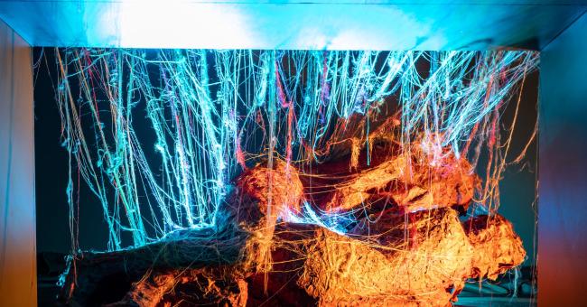 Fotografia instalacji: niebieskie pionowe światła i pomarańczowe ogniste smugi