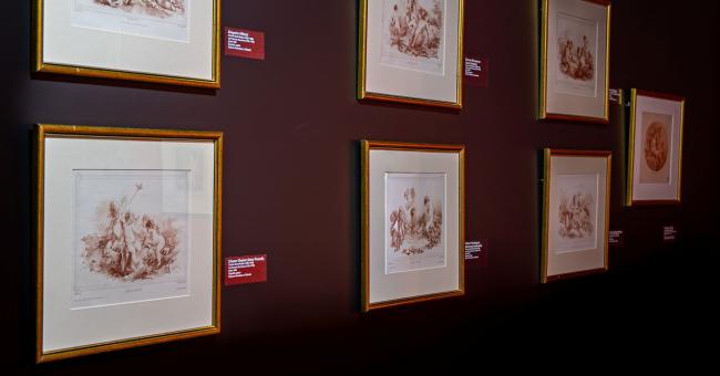 Seria rycin w złotych ramach na bordowej ścianie, czerwone etykiety