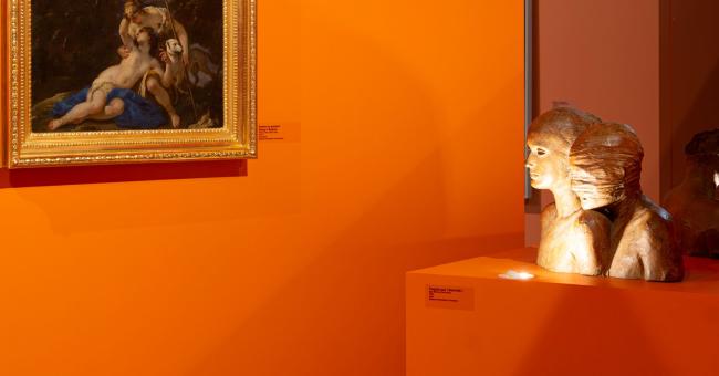 Sala muzealna z pomarańczową ścianą, obrazem w złotej ramie i rzeźbą na cokole