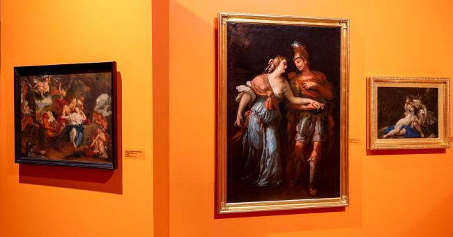 Fotografia trzech obrazów na pomarańczowej ścianie — centralny większy, boczne mniejsze