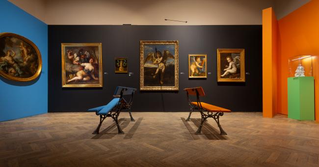 Fot. galerii, obrazy na ciemnej ścianie, dwa fotele (niebieski i pomarańczowy), zielony piedestał