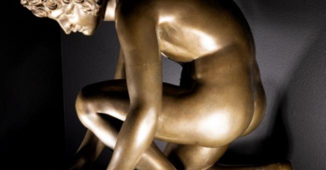 Fotografia złocistej rzeźby skrzydlatego młodzieńca klęczącego na okrągłej podstawie