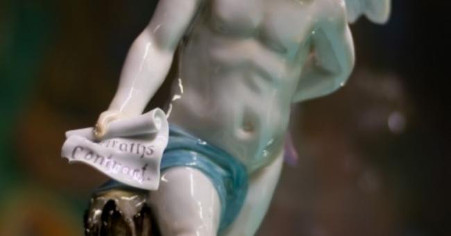 Zdjęcie porcelanowej figurki cherubina z kręconymi blond włoskami i niebieską przepaską