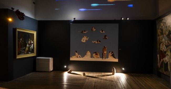 Fotografia sali galerii; ścienna instalacja z sylwetkami zwierząt, podświetlona ławka.