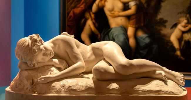 Fotografia marmurowej nagiej rzeźby leżącej na cokole, obraz w tle