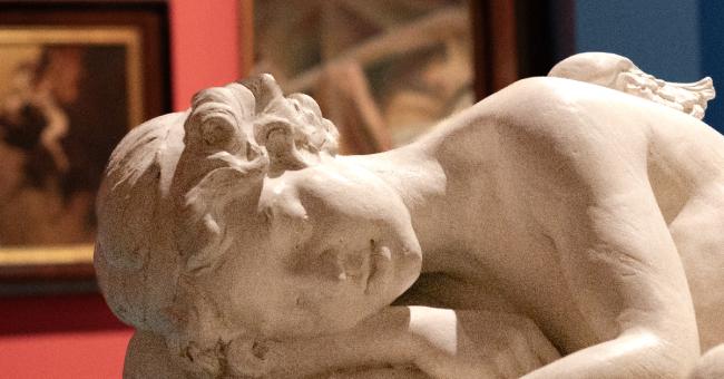 Fotografia marmurowej, leżącej rzeźby śpiącej kobiety w galerii na czerwonym tle