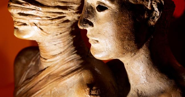 Fotografia dwóch popiersi: jedno z zabandażowaną głową, drugie kobiece, czerwone tło