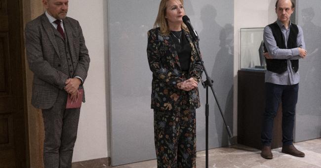 Fotografia trójki osób: kobieta przy mikrofonie, dwaj mężczyźni stoją obok