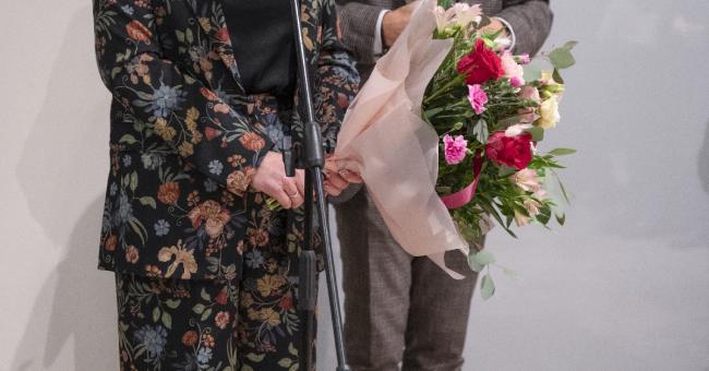 Fotografia: kobieta przy mikrofonie, mężczyzna obok trzyma bukiet kwiatów