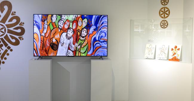 Fotografia wystawy: ekran z kolorową ilustracją na białych postumentach i przeszklona gablotka