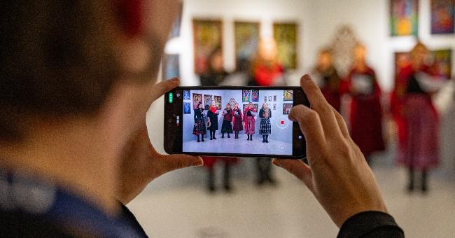 Fotografia: telefon rejestruje grupę osób w czerwonych strojach ludowych