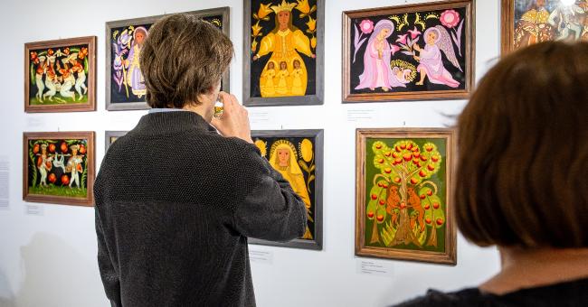 Fotografia: dwoje osób ogląda kolorowe, małe obrazy na białej ścianie we wnętrzach wystawy czasowej