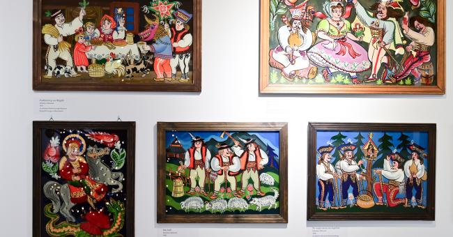 Pięć kolorowych, oprawionych malowideł na szkle z ludowymi scenami na białej ścianie