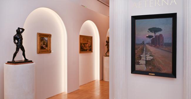 Fotografia galerii: białe arkady, kolumna z napisem, rzeźba na piedestale i obrazy na ścianach