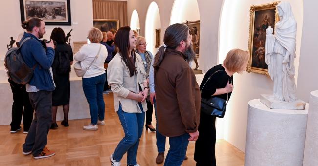 Fotografia: grupa osób ogląda marmurową rzeźbę i obrazy w jasnej galerii