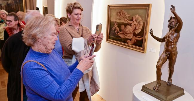 Fotografia: starsze kobiety fotografują brązową rzeźbę i obraz w jasnej galerii