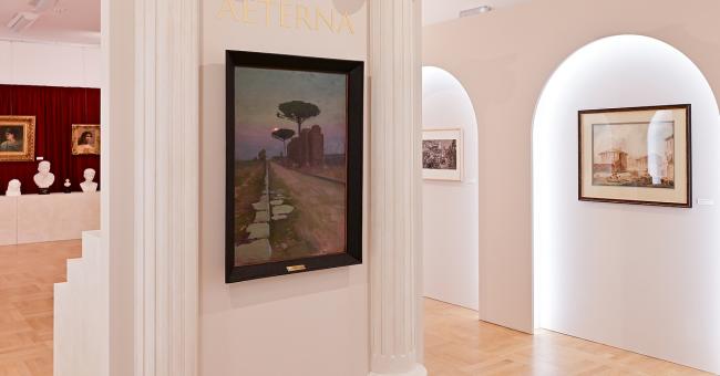 Fotografia galerii z białymi kolumnami, drewnianą podłogą i obrazami