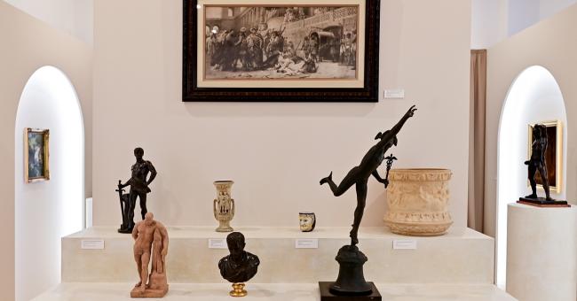 Fotografia galerii muzealnej z rzeźbami i wazonami na białych postumentach