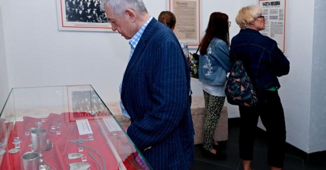 Fotografia mężczyzny w niebieskiej marynarce oglądającego eksponaty w szklanej gablocie w galerii