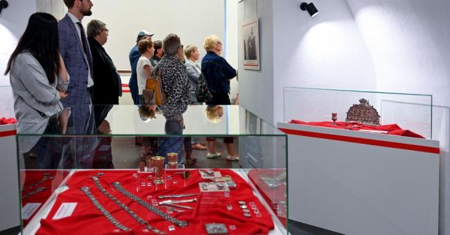 Zdjęcie: zwiedzający przy gablotach z zabytkami na czerwonym tle w białej sklepionej sali