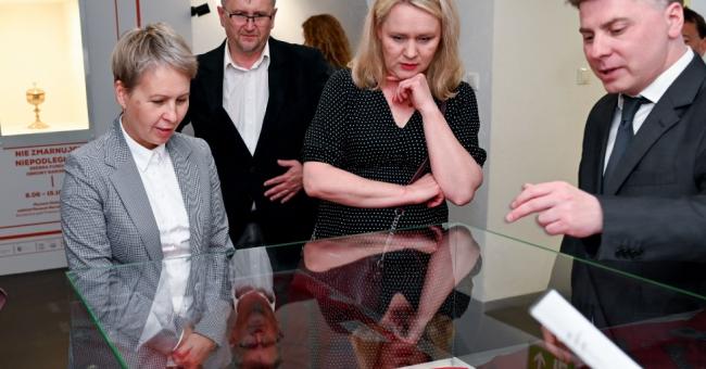 Fotografia: cztery osoby przy gablocie w galerii, mężczyzna wskazuje eksponat