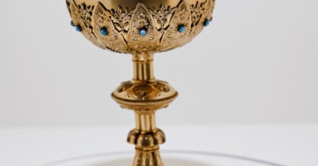 Fotografia złotego cyborium liturgicznego z wieczkiem i krzyżem na białym tle