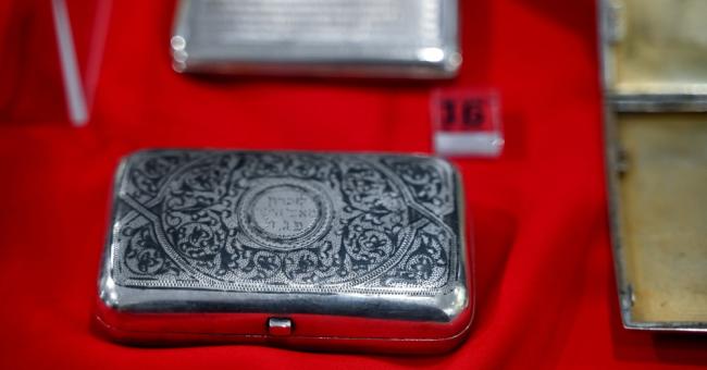 Fotografia srebrnej, grawerowanej papierośnicy na czerwonym tle