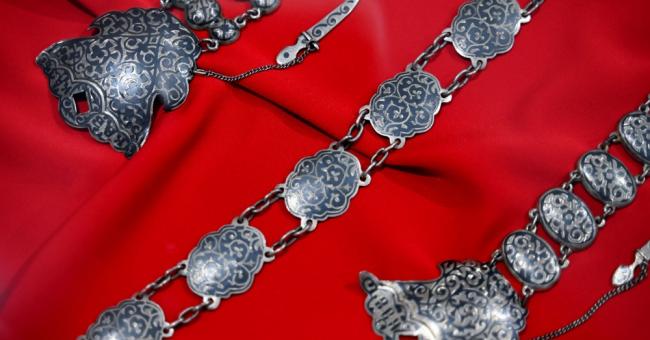 Fotografia srebrnej, zdobionej biżuterii na czerwonym jedwabistym tle