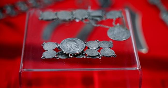 Fotografia: srebrny naszyjnik z wiszącymi medalionami na przezroczystej podstawce, czerwone tło