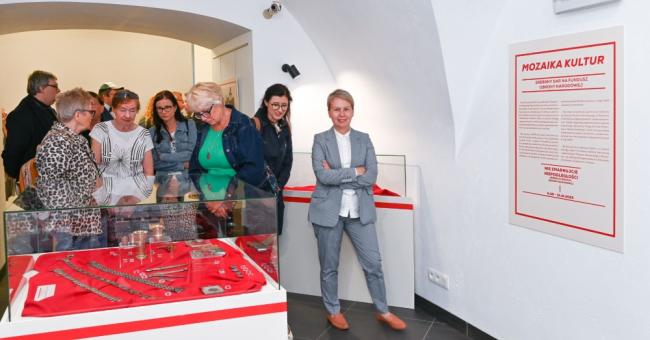 Fotografia: grupa zwiedzających przy czerwonych gablotach, obok stoi przewodnik w szarym garniturze