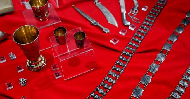 Fotografia: złote kielichy i drobna biżuteria (bransoletki, zegarek) na czerwonym tle