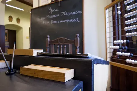 Fotografia wnętrza starej klasy z drewnianym biurkiem, czarną tablicą i liczydłem