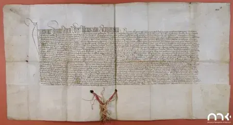 Pergaminowy akt z ręcznym pismem, zagięciami i wiszącą woskową pieczęcią