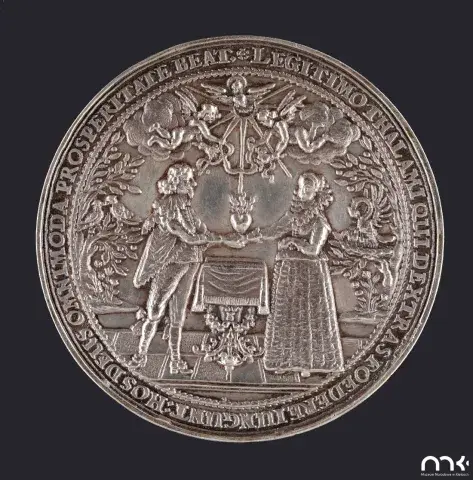 Zdjęcie srebrnego medalionu z reliefem: mężczyzna i kobieta trzymają serce nad stołem