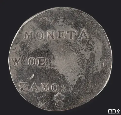 Fotografia starej posrebrzanej monety z napisem "MONETA W OBL ZAMOS" na ciemnym tle