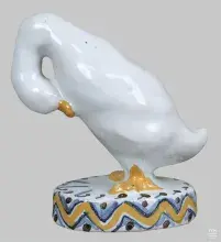 Fotografia ceramicznej białej kaczki z złotym dziobem i stopami na zdobionej podstawce