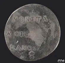 Fotografia starej posrebrzanej monety z napisem "MONETA W OBL ZAMOS" na ciemnym tle
